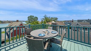 A balcony with a table and chairs, overlooking a residential area and a body of water. - Captain's Lookout | Roof Deck & Harbor Views (Gloucester)
