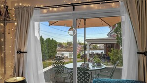 A room with a large window, a table with chairs, and a lamp. - Captain's Lookout | Roof Deck & Harbor Views (Gloucester)