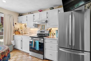 A kitchen with white cabinets, a stainless steel refrigerator, a stove, and a coffee maker.