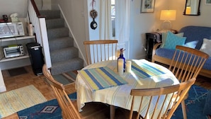 A dining area with a round table, wooden chairs, and a patterned tablecloth. - Captain's Lookout | Roof Deck & Harbor Views (Gloucester)