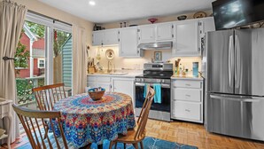 A kitchen with white cabinets, a stainless steel refrigerator, and a dining table with chairs. - Captain's Lookout | Roof Deck & Harbor Views (Gloucester)