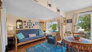 A cozy living room with a sofa, chairs, a dining table, and a view of the outdoors. - Captain's Lookout | Roof Deck & Harbor Views (Gloucester)