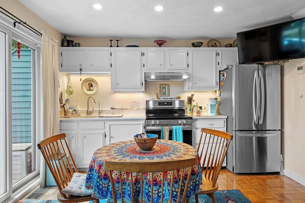A kitchen with white cabinets, a stainless steel refrigerator, and a dining table with a colorful tablecloth.
