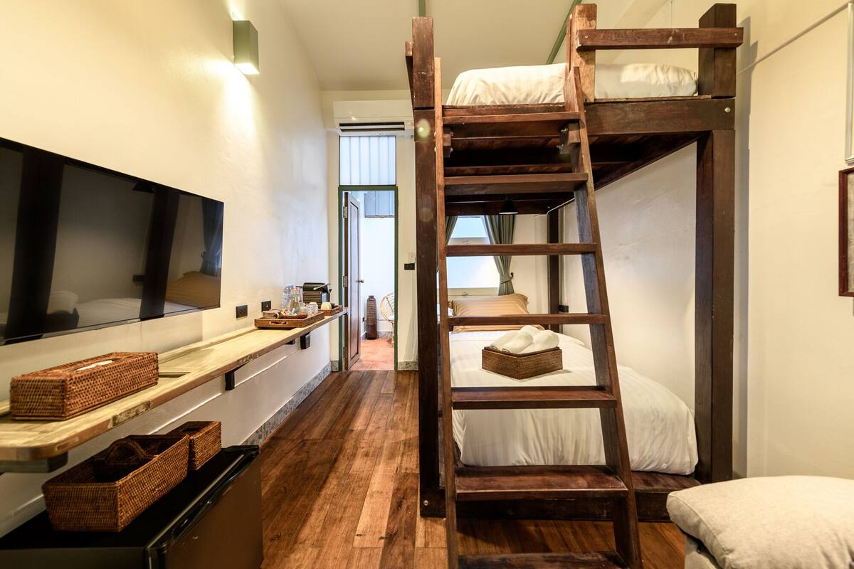 A bunk bed room with a wooden ladder, a flat-screen TV, and a wooden shelf with baskets.