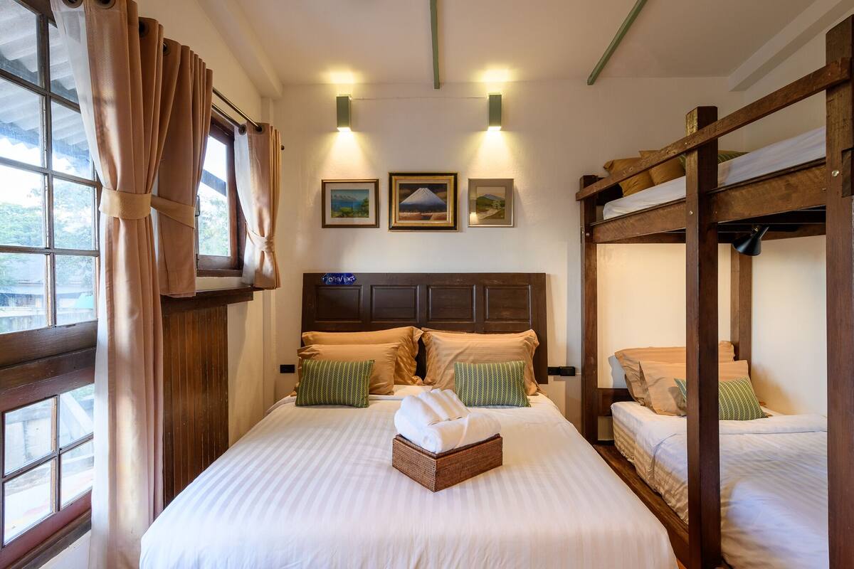 A room with a large bed, two smaller beds, a window with curtains, and wall-mounted lights.