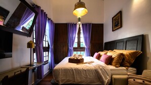 A bedroom with a bed, a bedside table, a lamp, a window with curtains, and a painting on the wall. - Hanuman Boutique Stay & Eatery (Hat Yai)