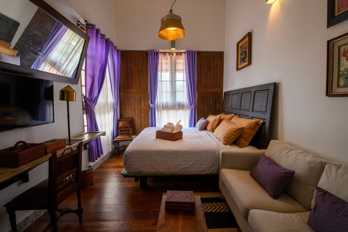 A hotel room with a bed, a sofa, a TV, a lamp, and a window with curtains.