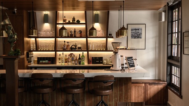 A bar area with wooden bar stools, shelves with bottles, glasses, and a sign. - Hanuman Boutique Stay & Eatery (Hat Yai)