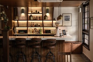 Eine Bar mit Holzhockern, Regalen voller Flaschen und Gläsern sowie einem Schild.