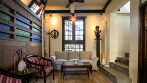 A cozy living room with a sofa, armchair, and coffee table. There is a wooden wall with glass panels, a fireplace, and a staircase. - Hanuman Boutique Stay & Eatery (Hat Yai)