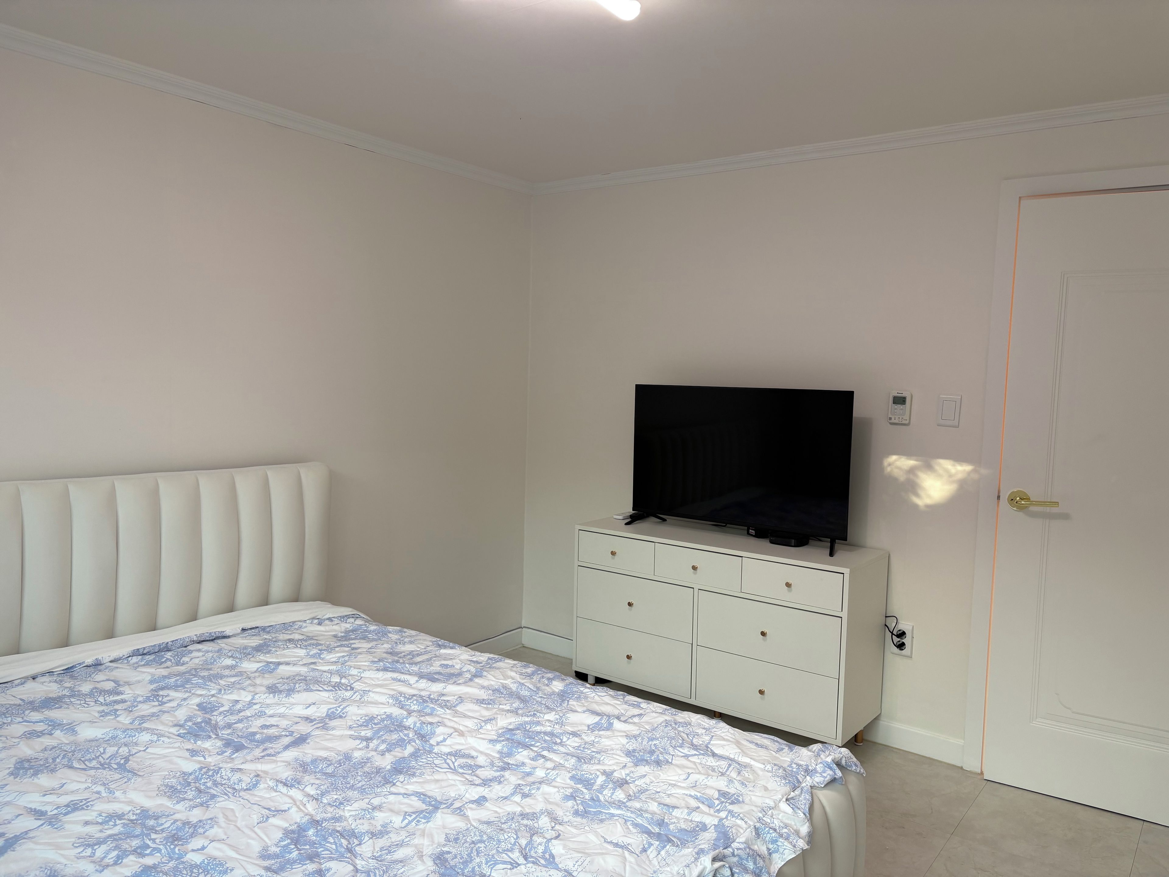 A bedroom with a bed, a dresser, a television, and a door.