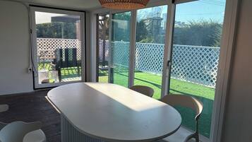 A room with a large table and chairs, a wicker ceiling light, and a sliding glass door leading to a fenced outdoor area.