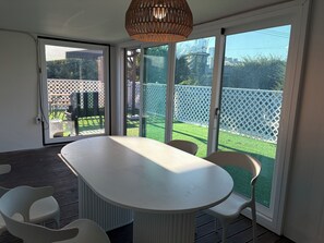 A room with a large table and chairs, a wicker ceiling light, and a sliding glass door leading to a fenced outdoor area.