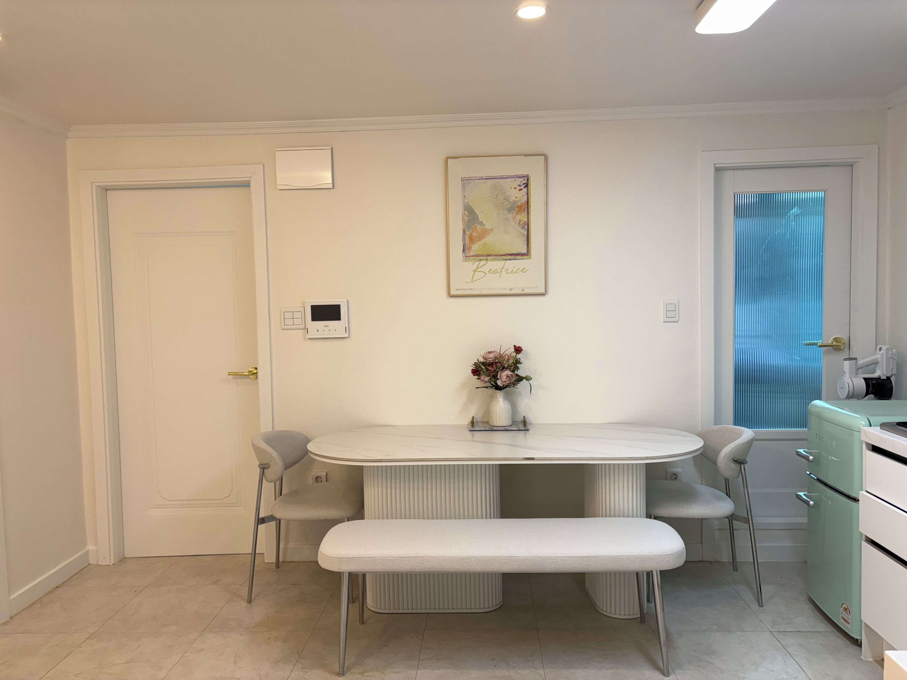 Una cocina moderna con una mesa de comedor, sillas, un banco, un refrigerador y una ventana con cortinas.