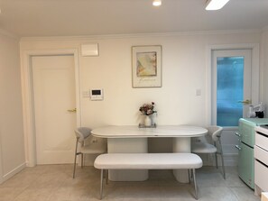 Eine moderne Küche mit Esstisch, Stühlen, einer Bank, einem Kühlschrank und einem Fenster mit Vorhängen.