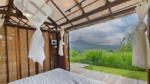 A bedroom with a large bed, wooden walls, and a view of a lush garden and mountains. - Calidas Hill (Kintamani)