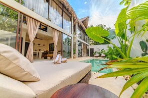 A modern outdoor living area with a pool, a sofa, and a dining area visible through large windows. - Design Villa With Palapa Roofs, High Ceilings and 9 Meters private Pool (Tulum)