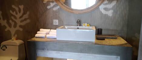A bathroom with a rectangular sink, white towels, a toilet, and a window with a wooden frame.