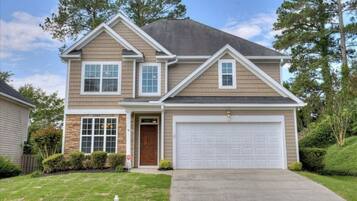 A two-story house with a garage, a stone foundation, and a well-maintained lawn.