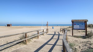 A wooden boardwalk leading to a beach with a lifeguard station and a signboard.