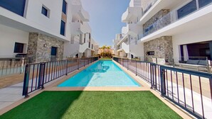 A modern hotel with a central swimming pool, surrounded by balconies and a stone facade.