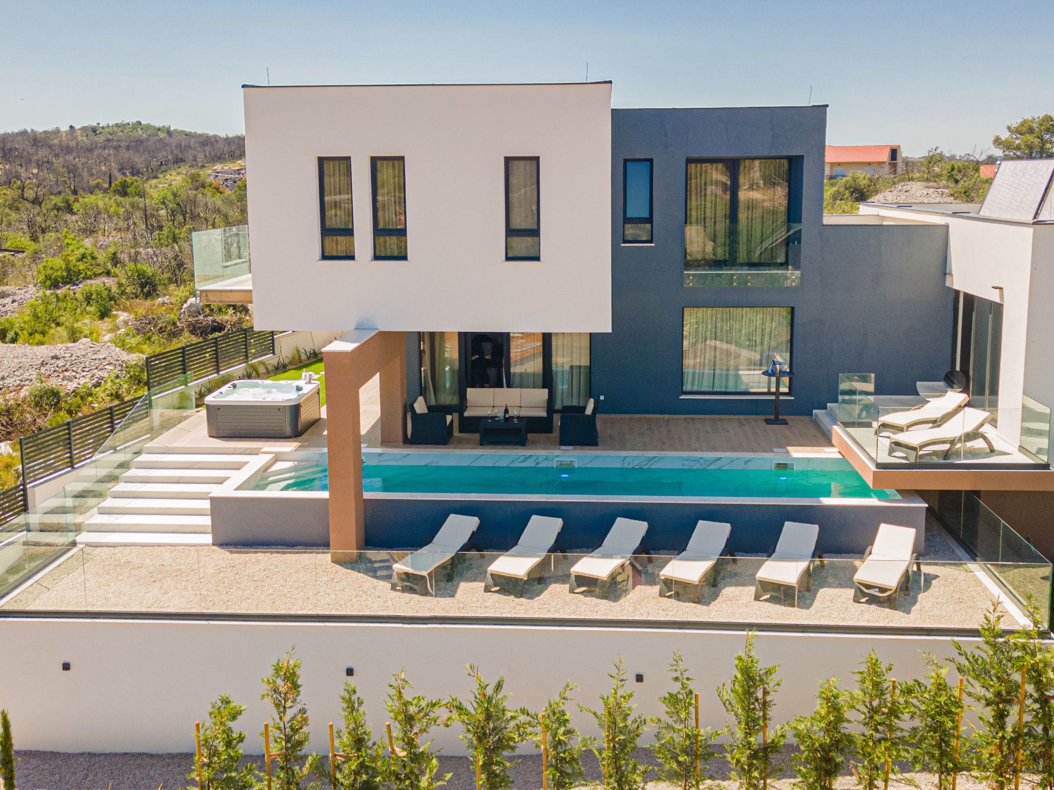 Una casa moderna de dos pisos con piscina, mobiliario exterior y vista del paisaje circundante.