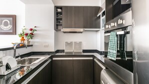 A modern kitchen with dark wood cabinets, stainless steel appliances, and a black countertop. - Departamento en Punta del Este (Punta del Este)