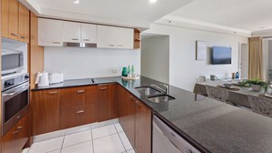 A modern kitchen with wooden cabinets, stainless steel appliances, and a granite countertop. - Chevron Renaissance Ocean View (Surfers Paradise)