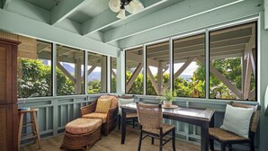 A covered porch with wicker furniture, large windows, and a view of greenery. - Paradise at Prettyville Kauai, waterfall & ocean View, AC, sleep 8-10, BigAloha (Princeville)