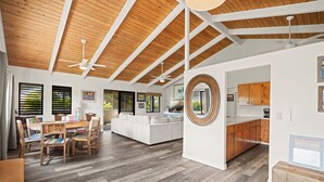 A spacious living area with a wooden ceiling, a dining table with chairs, a sofa, and a kitchen area with wooden cabinets. - Paradise at Prettyville Kauai, waterfall & ocean View, AC, sleep 8-10, BigAloha (Princeville)