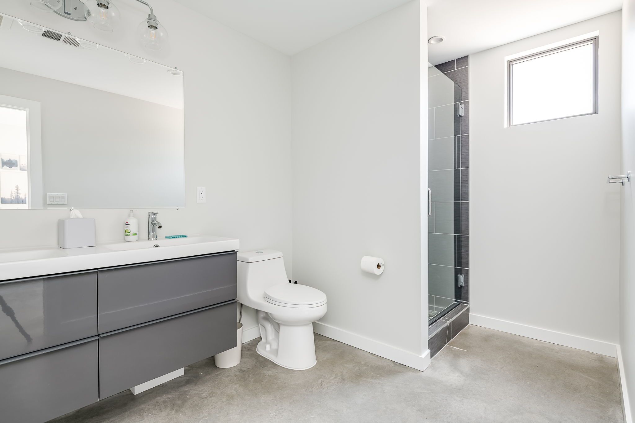 A modern bathroom with a white vanity, a toilet, and a glass shower enclosure.