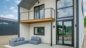Una casa moderna de dos pisos con un balcón, un sofá seccional gris y un amplio ventanal corredera.