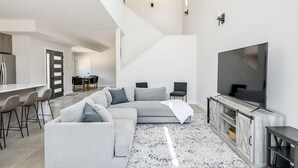 Una sala de estar moderna con un sofá modular, un televisor de pantalla plana y una escalera que sube a un nivel superior.