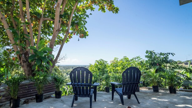 Two black chairs and a small table on a concrete patio with potted plants and a view of the landscape. - Cozy two bedroom house with a Million dollar view, Arroyo, Puerto Rico. (Arroyo)
