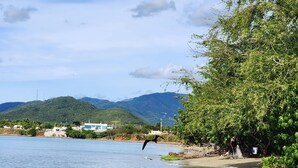 A beach with a clear view of the water, a person fishing, and a boat in the background. - Cozy two bedroom house with a Million dollar view, Arroyo, Puerto Rico. (Arroyo)
