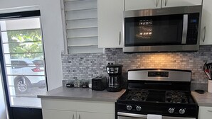 A modern kitchen with white cabinets, a stainless steel stove, a microwave, and a coffee maker. - Cozy two bedroom house with a Million dollar view, Arroyo, Puerto Rico. (Arroyo)