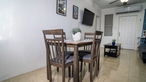 A dining area with a wooden table and chairs, a potted plant, and a television mounted on the wall. - Cozy two bedroom house with a Million dollar view, Arroyo, Puerto Rico. (Arroyo)