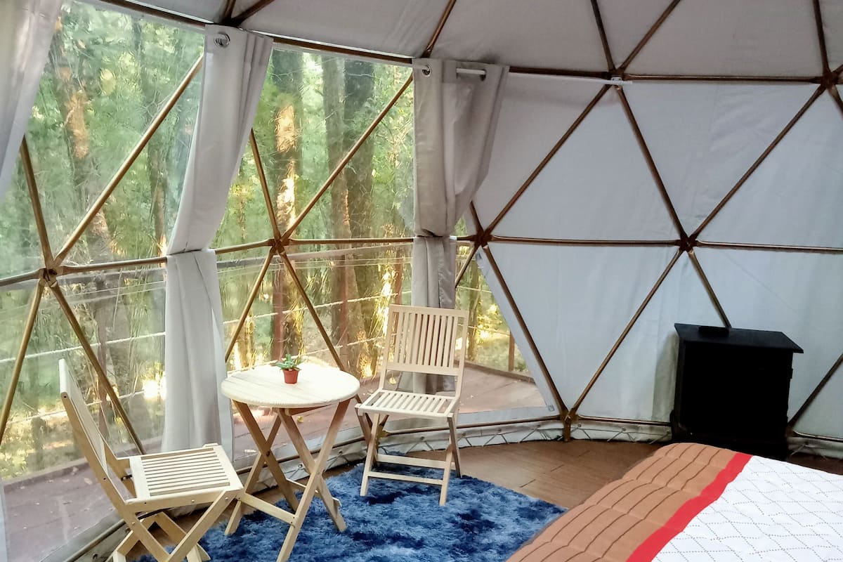 A tented room with a bed, a small table, two chairs, and a blue rug.