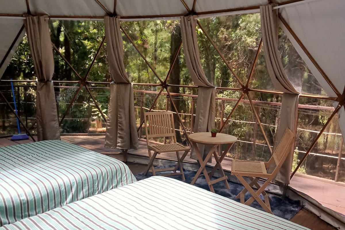 A tented accommodation with two beds, a small table, and a chair.