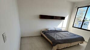 Een slaapkamer met een bed, een raam en een blauwe mand.