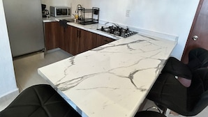 Een moderne keuken met een marmeren aanrechtblad, houten keukenkastjes, een ingebouwde oven en een gasfornuis.
