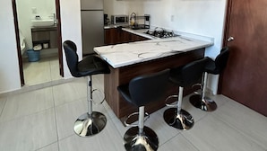 Een compacte keuken met een centraal eiland, vier barkrukken en houten kastjes.