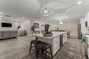 A spacious kitchen with a central island, modern pendant lighting, and a dining area with a large table and chairs. - Gem in a box! (Fredericksburg)