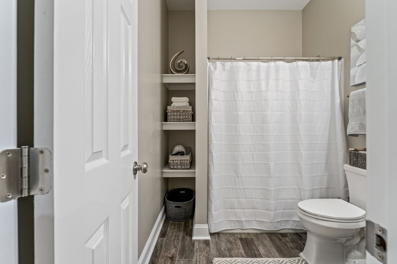 A bathroom with a white toilet, a shower curtain, and shelves with towels and baskets.