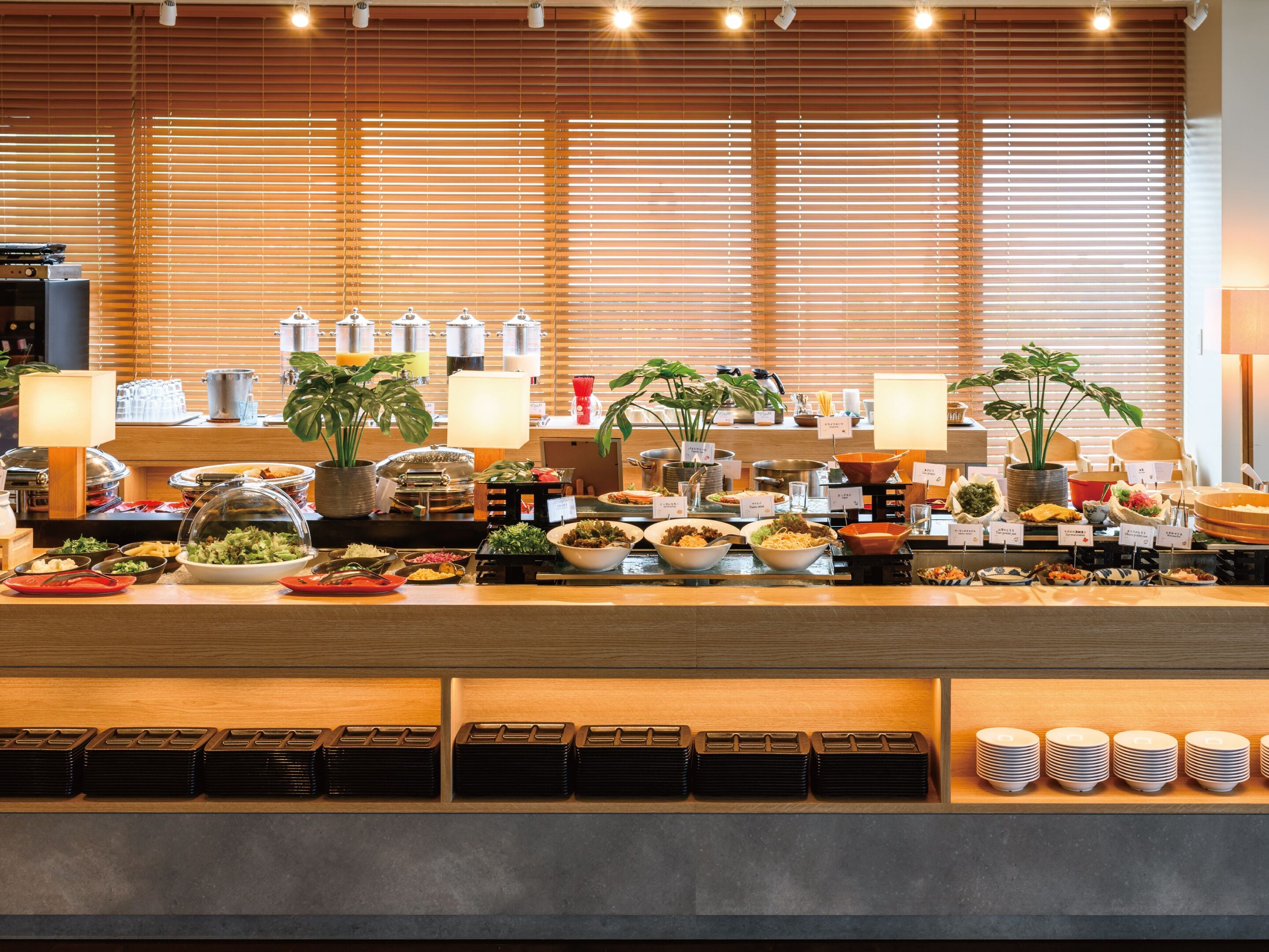 Disposición de buffet con diversos platos, una estación de café y plantas en macetas.