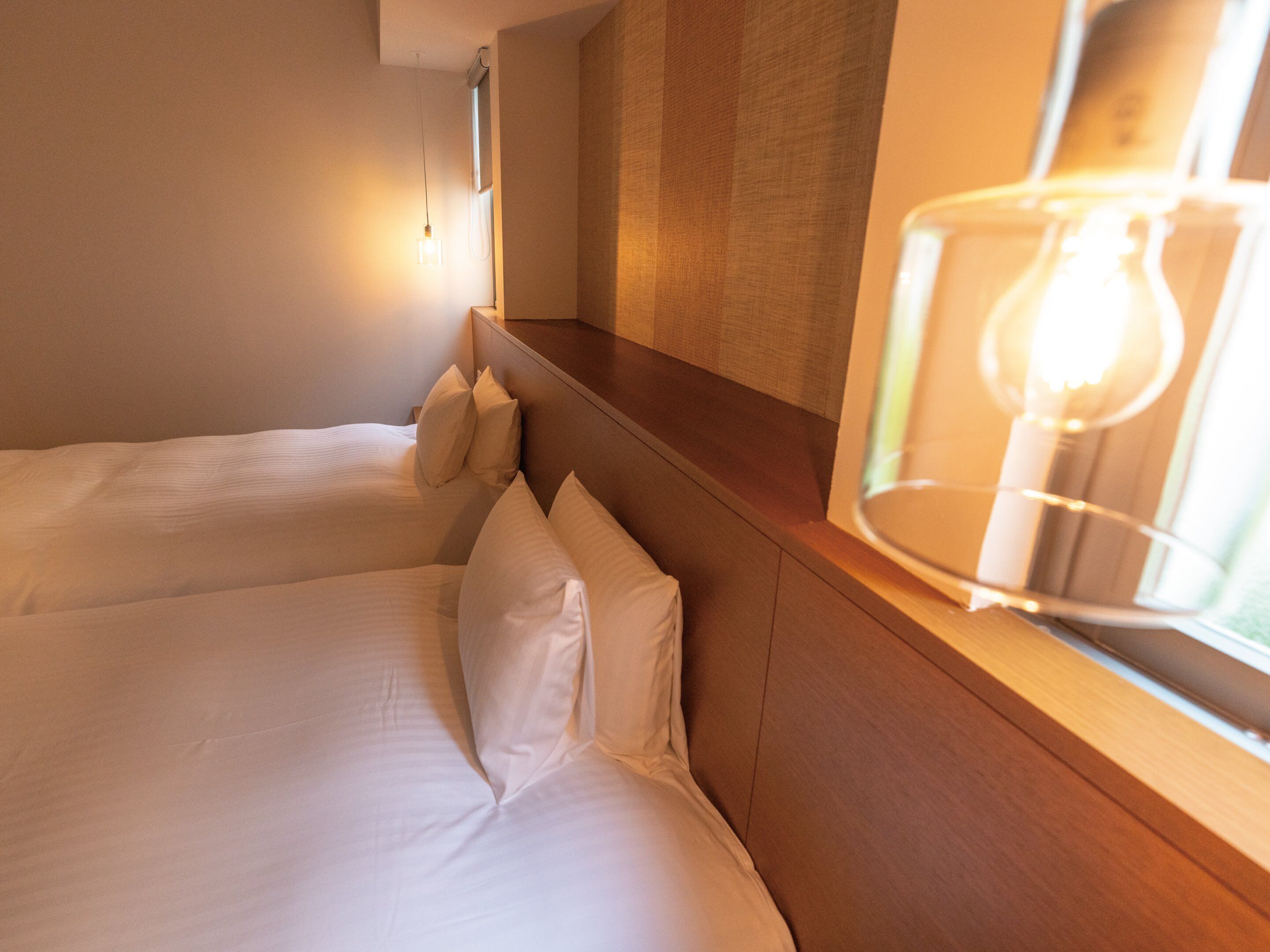 Une chambre d’hôtel avec deux lits, une tête de lit en bois, une fenêtre avec un luminaire et un climatiseur fixé au mur.