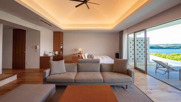 A modern hotel room with a large bed, a sofa, a coffee table, and a view of the sea.