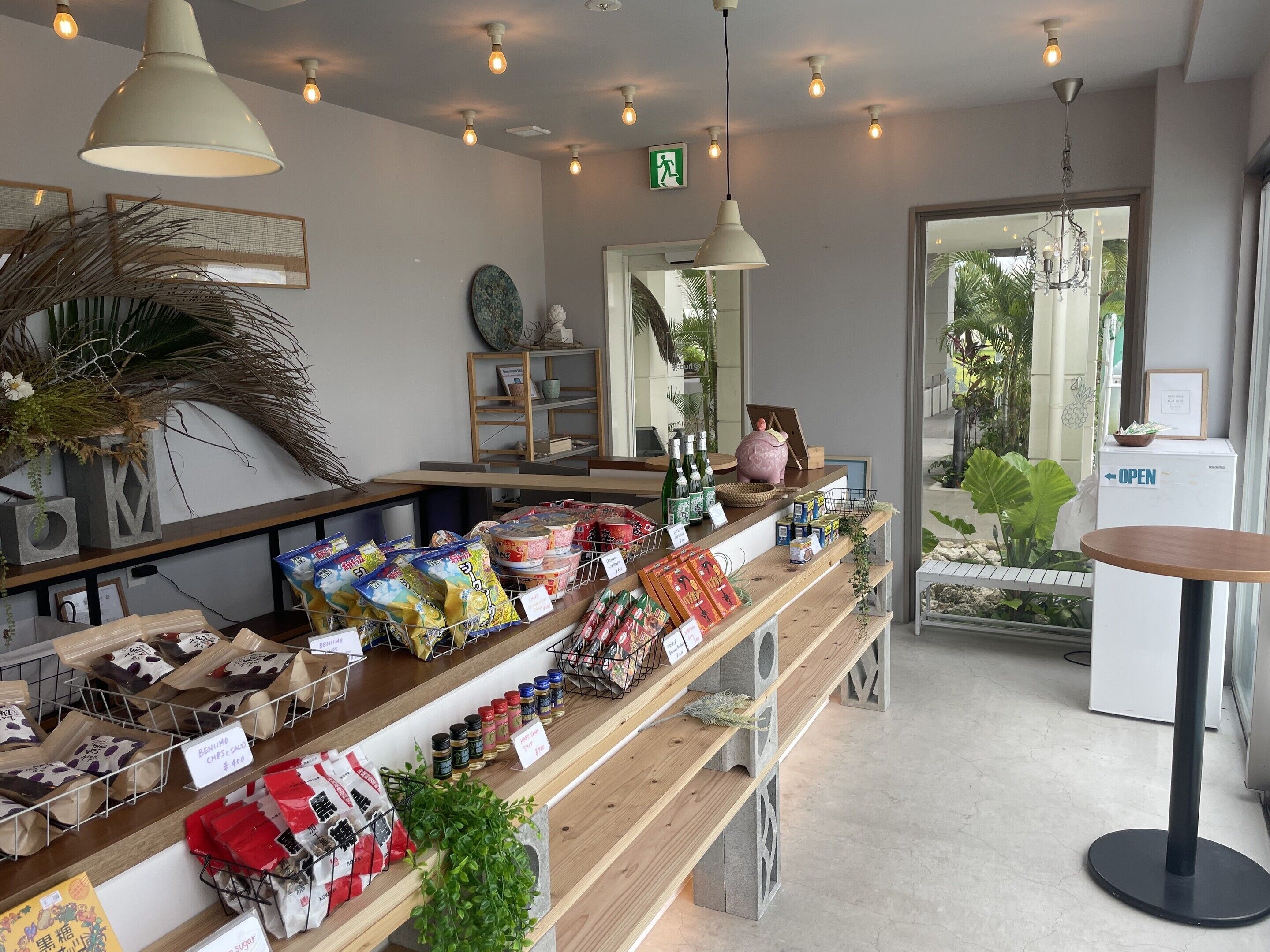 Interior de una tienda con estantes llenos de productos envasados, un mostrador con caja registradora y una puerta que indica 'ABIERTO'.