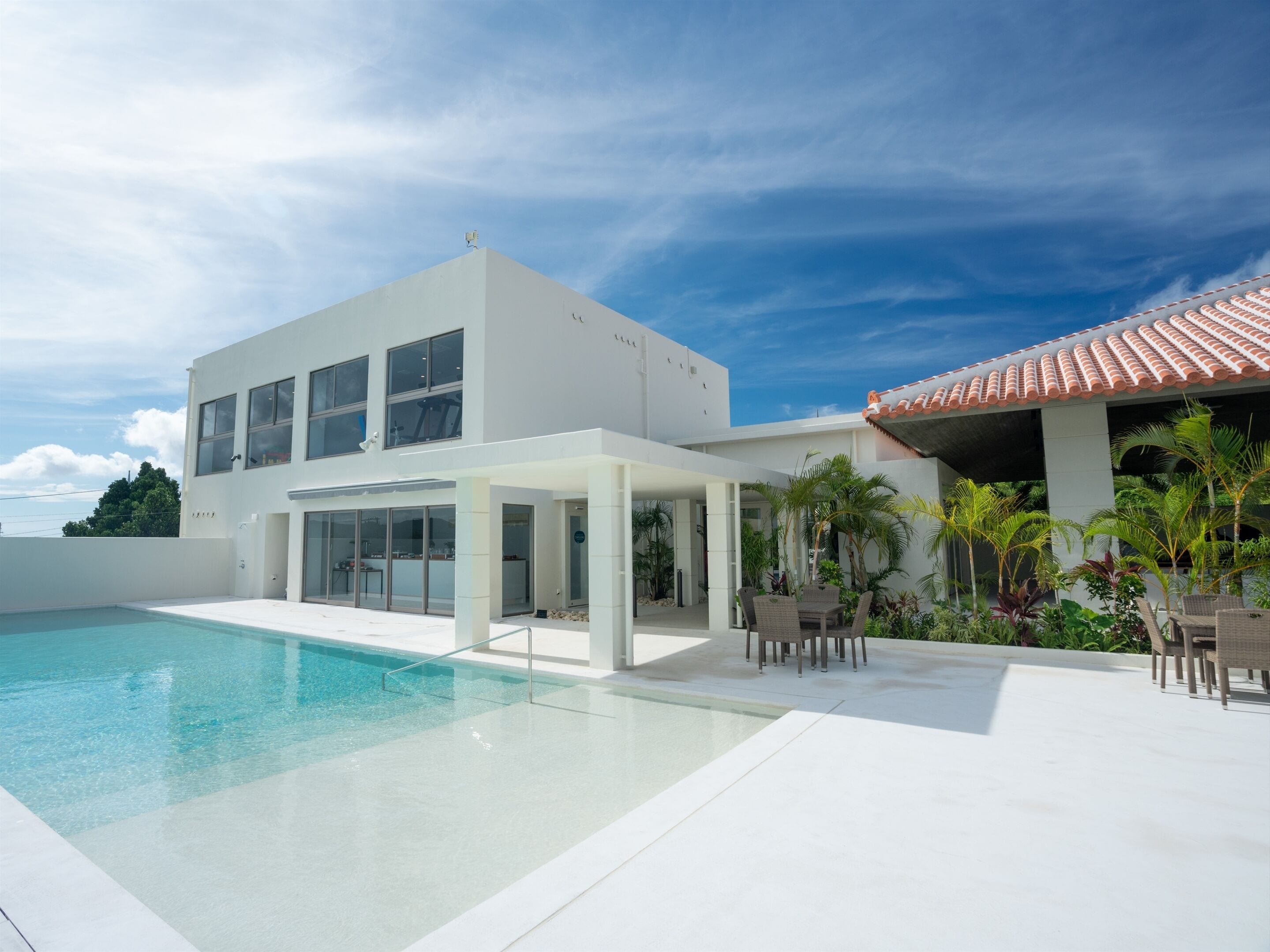 Una casa moderna con piscina, mobiliario de exterior y un patio cubierto.