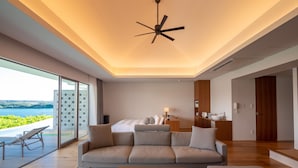 A modern hotel room with a large bed, a sofa, a dining area, and a view of the sea.